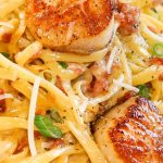 linguine pasta in a creamy carbonara sauce topped with pan seared scallops and green onion slices.