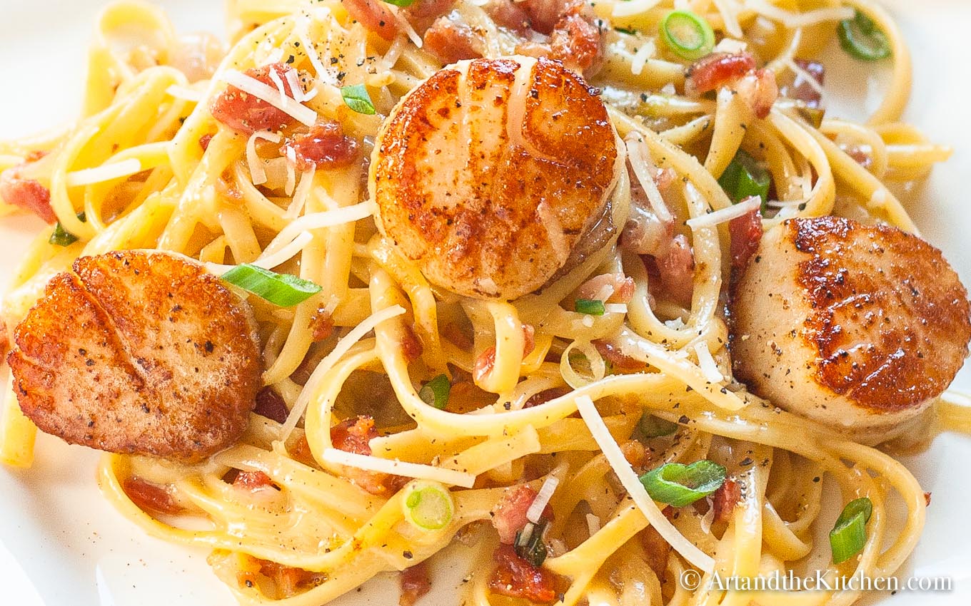 linguine pasta in a creamy carbonara sauce topped with pan seared scallops and green onion slices.