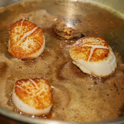 Three golden brown scallops frying in pan.