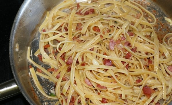 skillet with cooked linguine pasta tossed with bacon and onions
