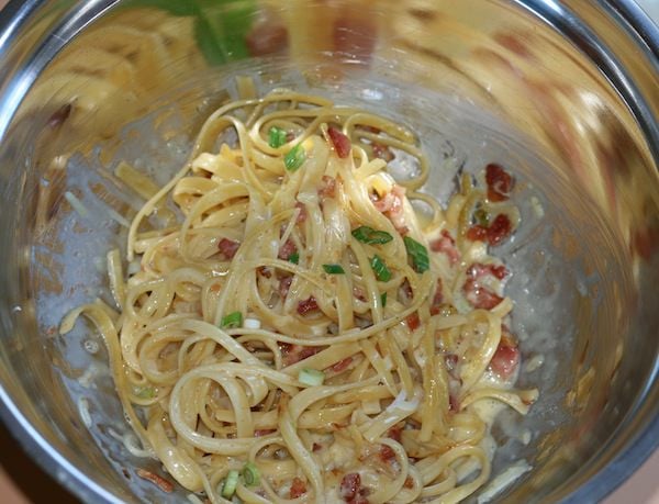 stainless steel mixing bowl filled with linguine, tossed in carbonara sauce
