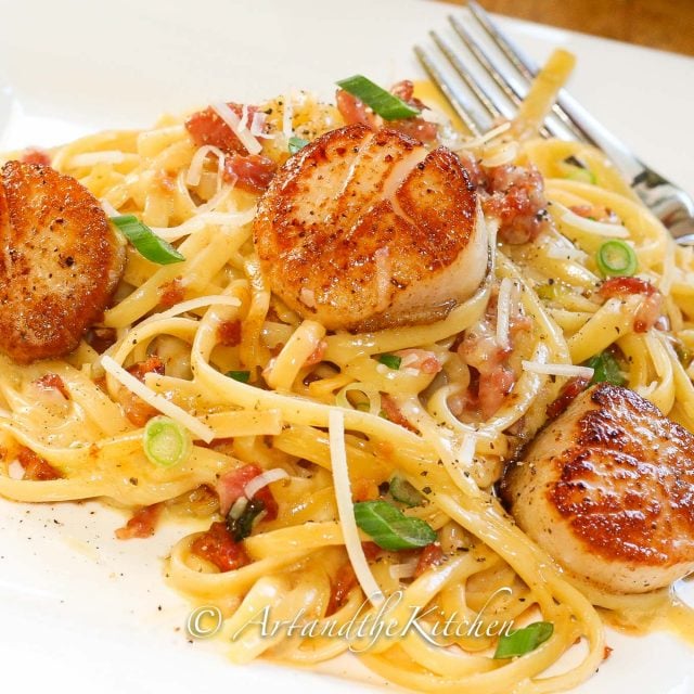 linguine pasta in a creamy carbonara sauce topped with pan seared scallops and green onion slices.