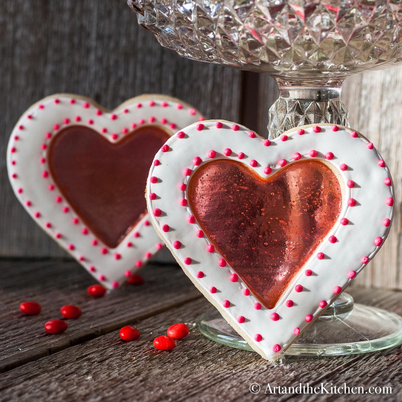 Two heart shaped cookies decorated with a red stained glass looking center.