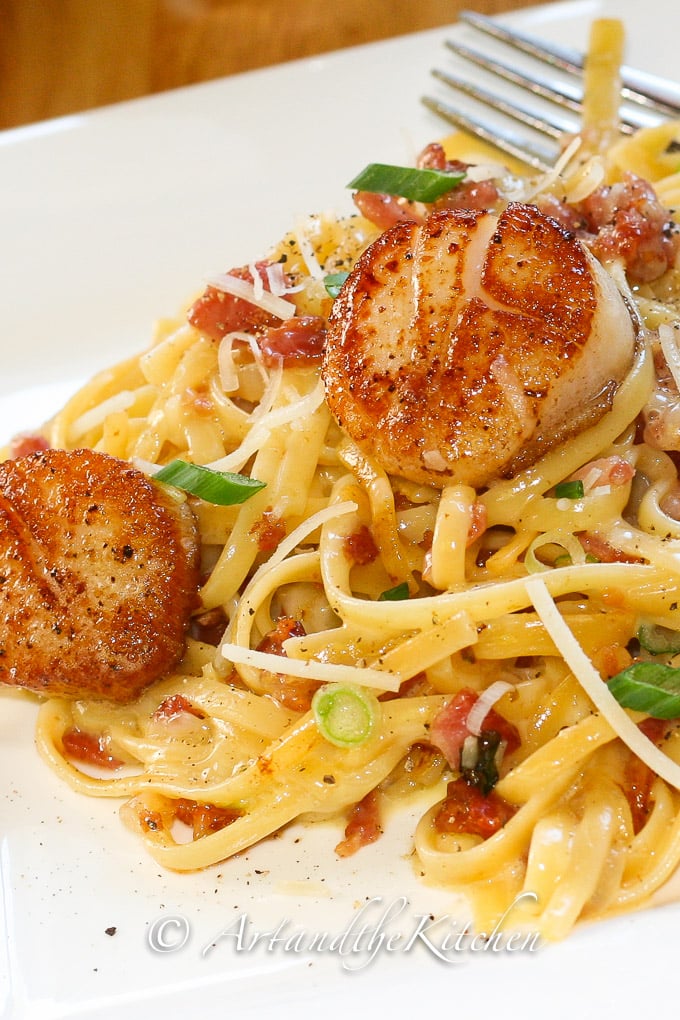 linguine pasta in a creamy carbonara sauce topped with pan seared scallops and green onion slices.