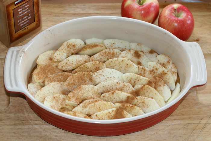 Oval baking dish filled with slices of apple sprinkled with cinnamon.