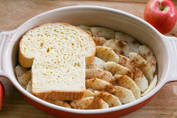 Oval baking dish filled with apple slices, covered with a slice of unbaked egg coated bread.