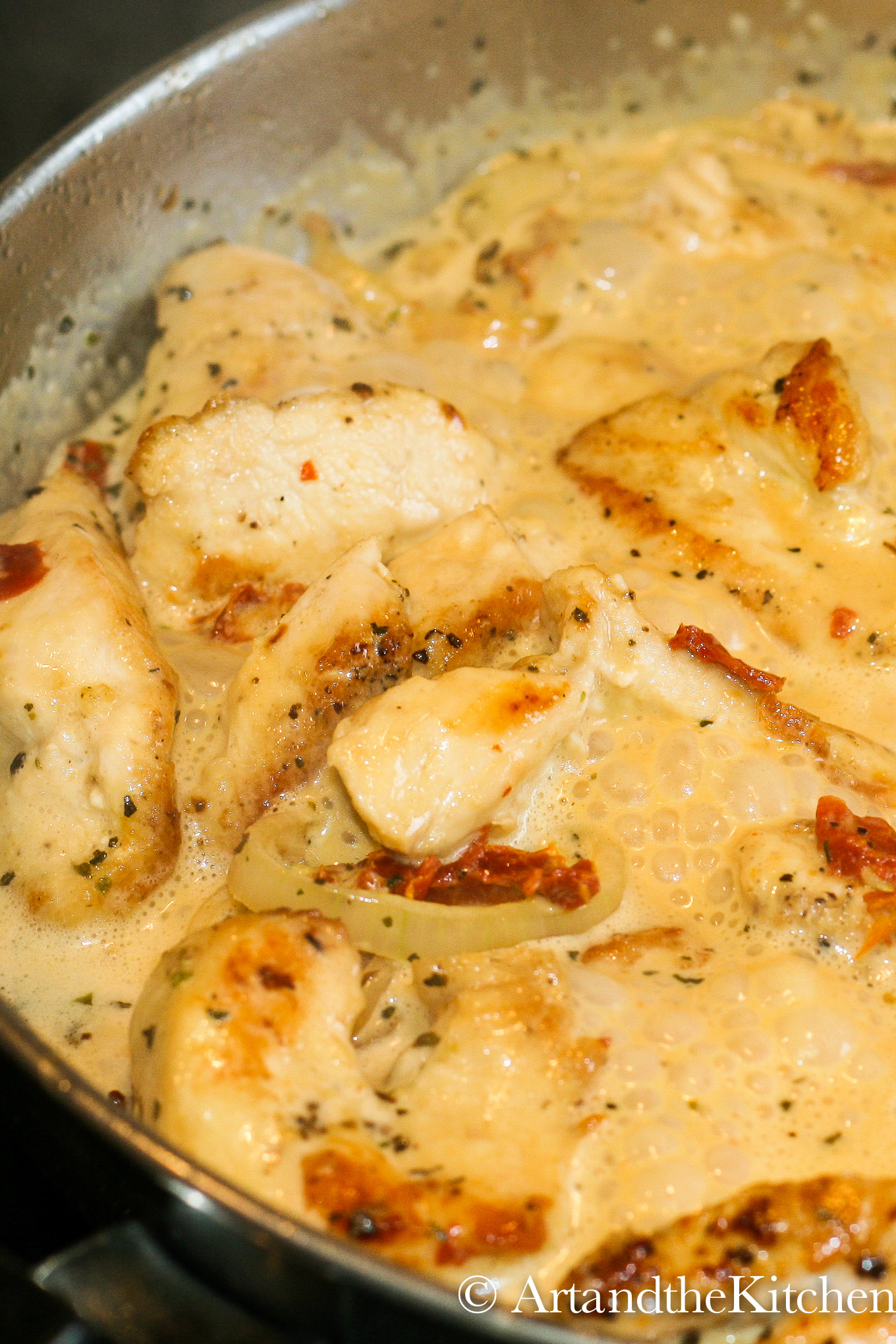 chicken with shallots and sun-dried tomatoes in a creamy sauce simmering in a stainless steel skillet.