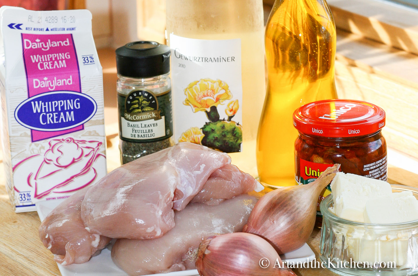 ingredients on wood board chicken breasts, cream, shallots, butter, white wine, sun-dried tomatoes, basil and olive oil.