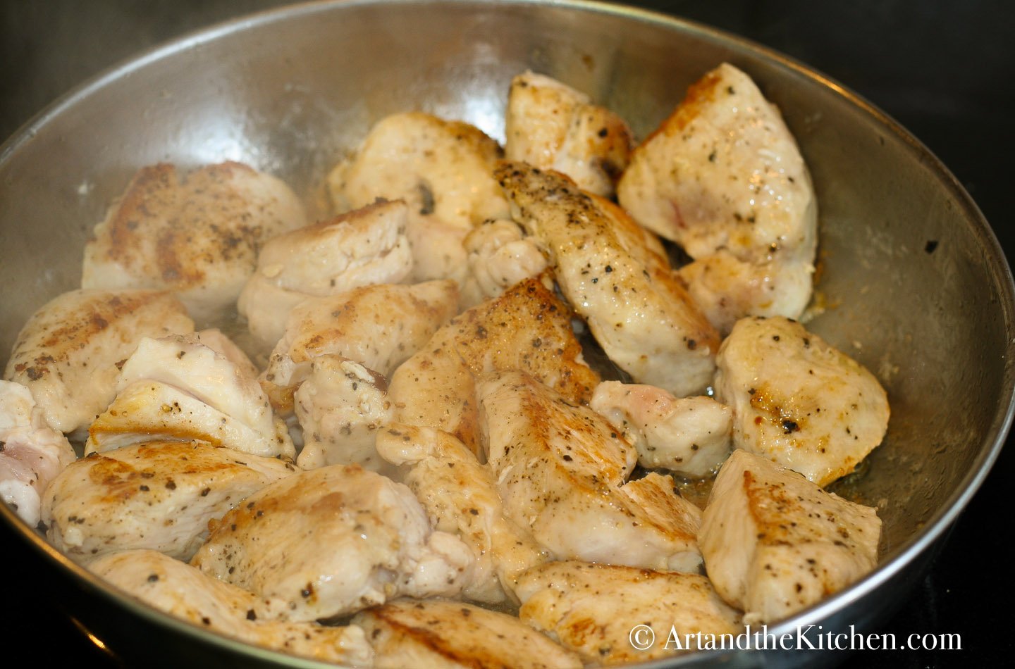 chopped up chicken frying in stainless steel skillet.