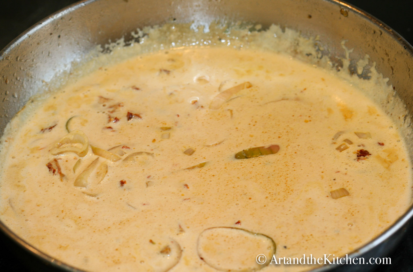 Sauce of sun-dried tomatoes, shallots, white wine and cream simmering in skillet.