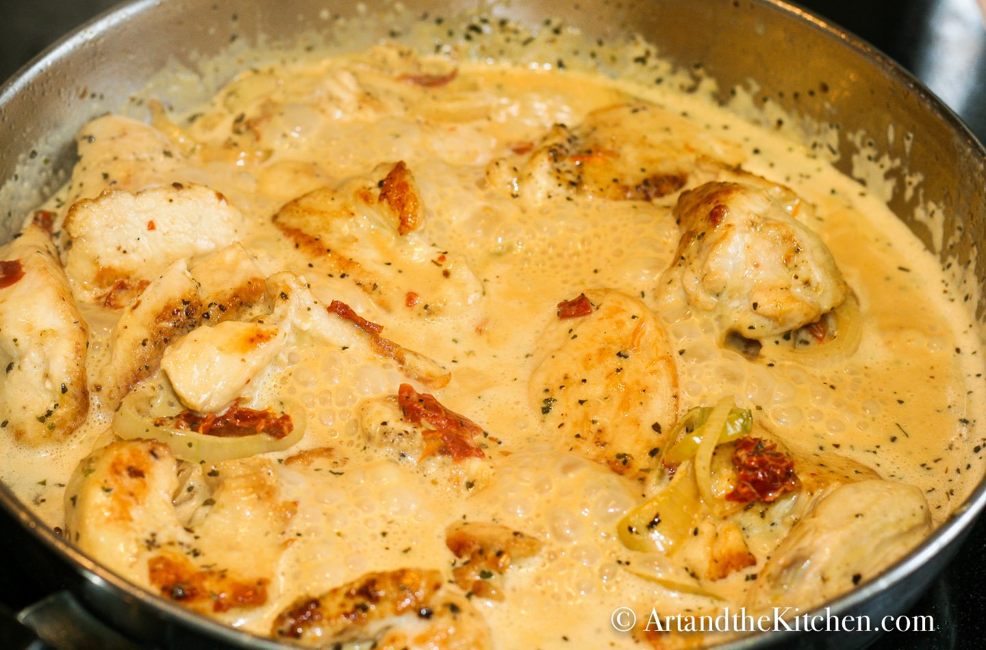 Chicken in a creamy sun-dried tomato sauce simmering in a stainless steel skillet.
