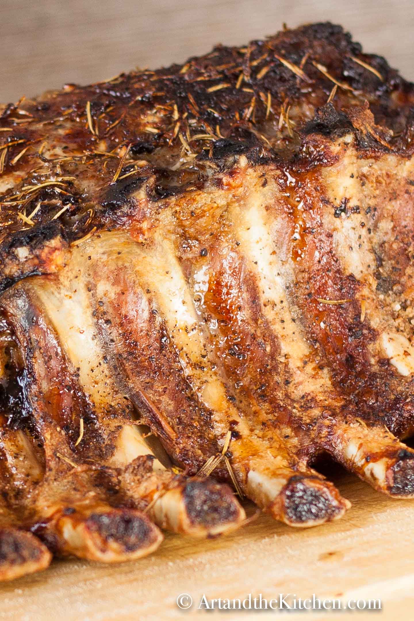 Cooked whole pork rib roast topped with herbs on wood cutting board.