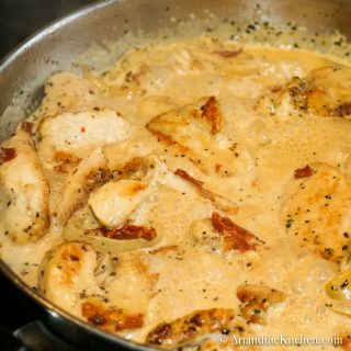 chicken with shallots and sun-dried tomatoes in a creamy sauce simmering in a stainless steel skillet.