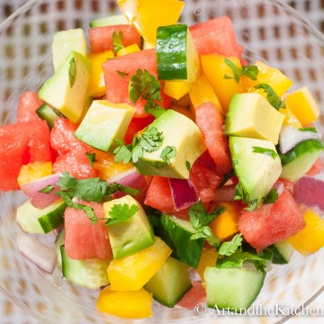 Salad of avocado, watermelon, cucumber, peppers, and red onions in glass bowl.