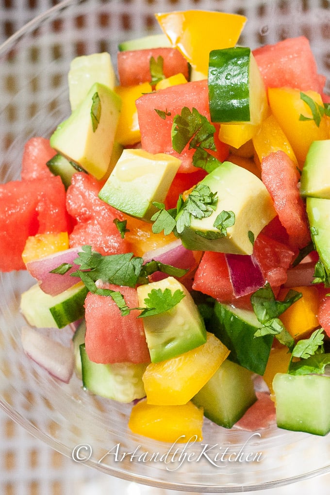 Salad of avocado, watermelon, cucumber, peppers, and red onions in glass bowl.
