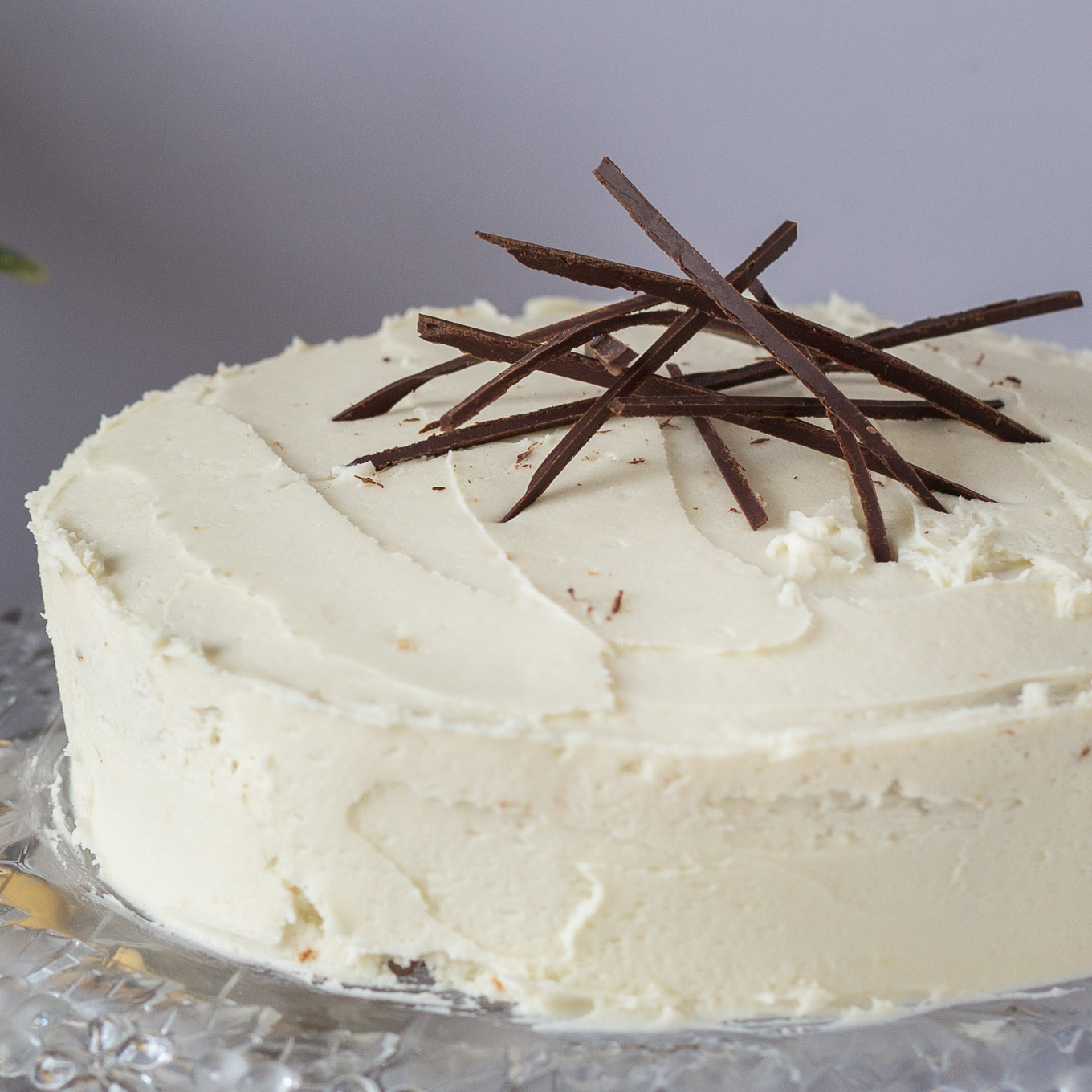 Whole banana cake covered with cream cheese frosting, topped with thin chocolate sticks.