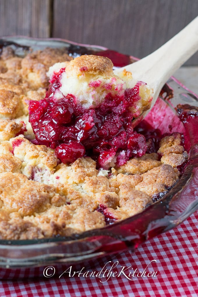 Cobbler made with sour cherries in a glass pie plate scooped out with wooden spoon