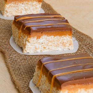 Row of Rice Krispie treats with layers of caramel and chocolate.