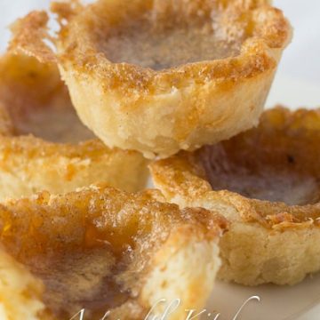Stack of four butter tarts on white plate.