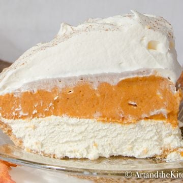 Slice of pumpkin pie with layers of pumpkin, cream cheese and whipped cream on amber coloured glass plate.