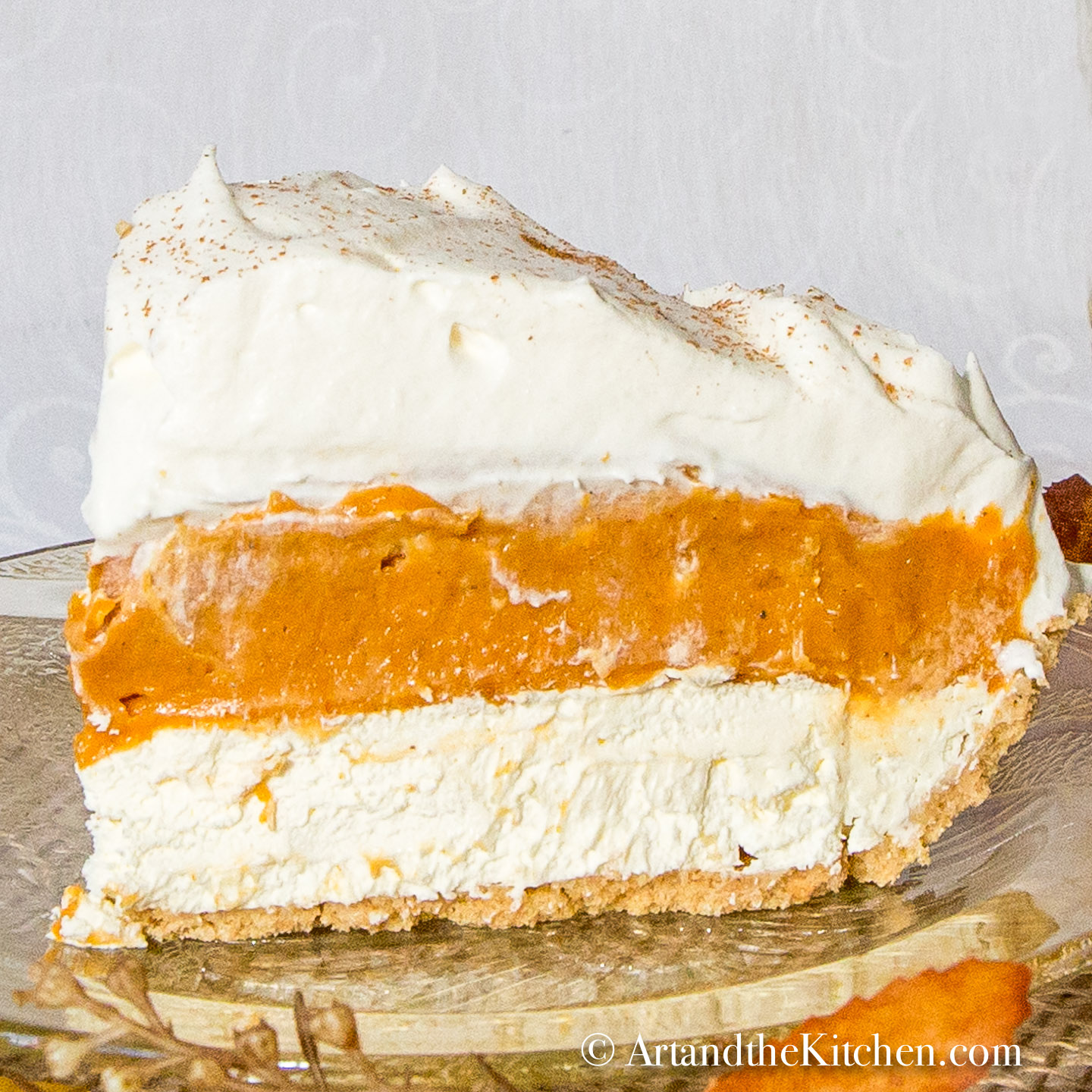 Slice of pumpkin pie with layers of pumpkin, cream cheese and whipped cream on amber coloured glass plate.