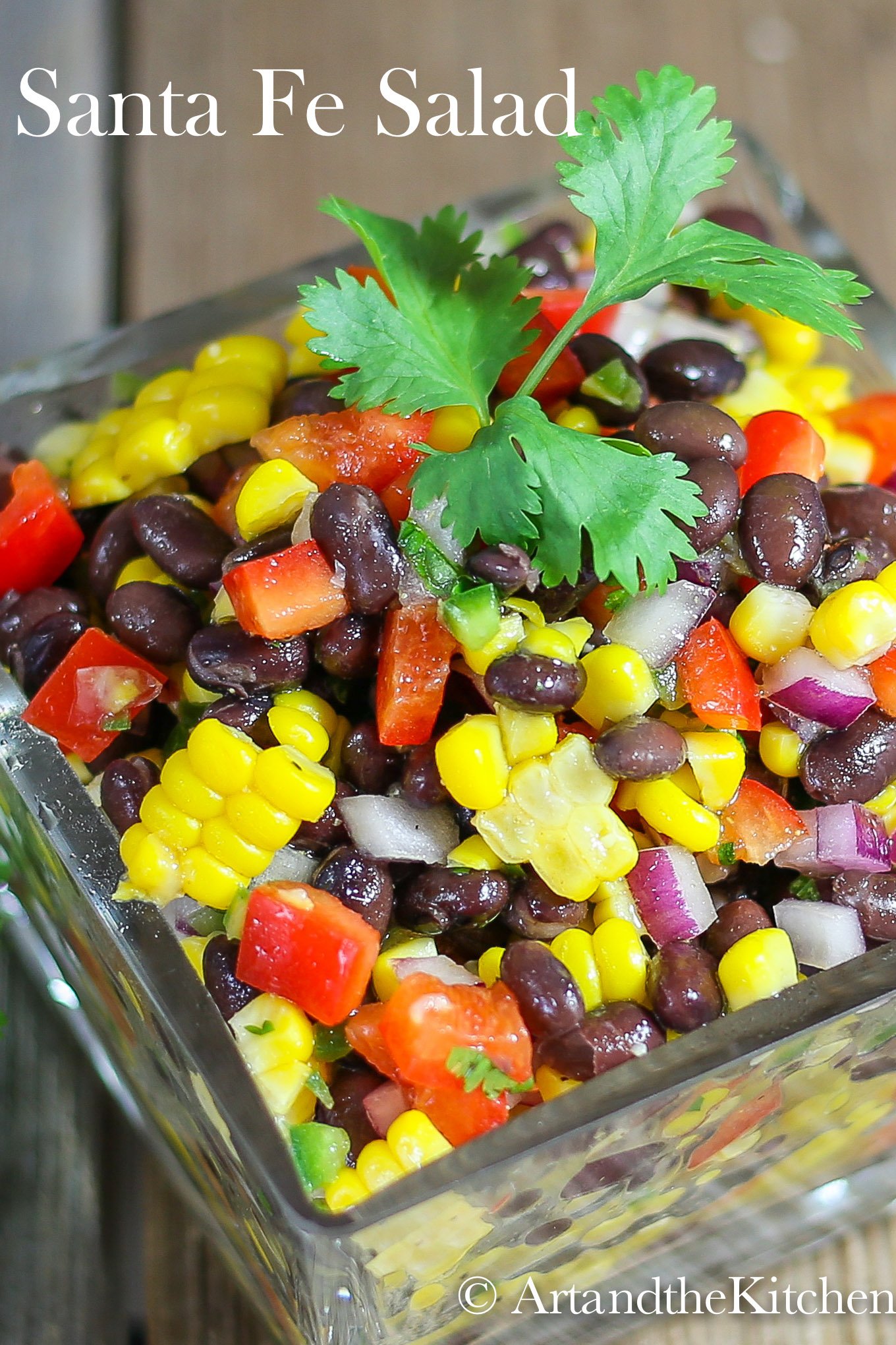 Glass bowl filled with salad of black beans, corn red , pepper, red onions and jalapeño. Garnished with parsley sprig.