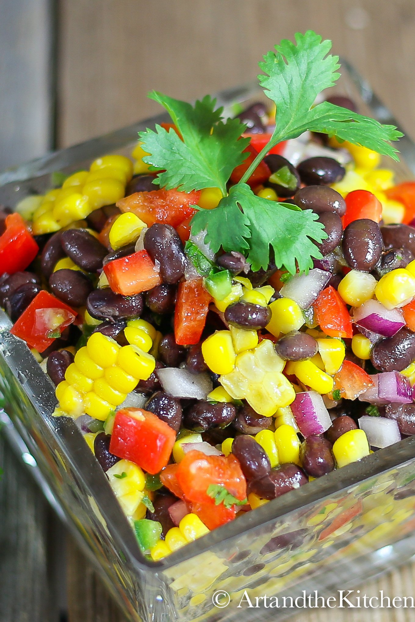 Glass bowl filled with Santa fe salad made with black beans, corn red , pepper, red onions and jalapeño. Garnished with parsley sprig.