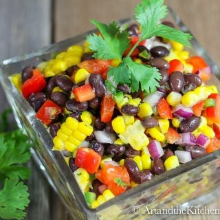 Glass bowl filled with salad of black beans, corn red , pepper, red onions and jalapeño. Garnished with parsley sprig.