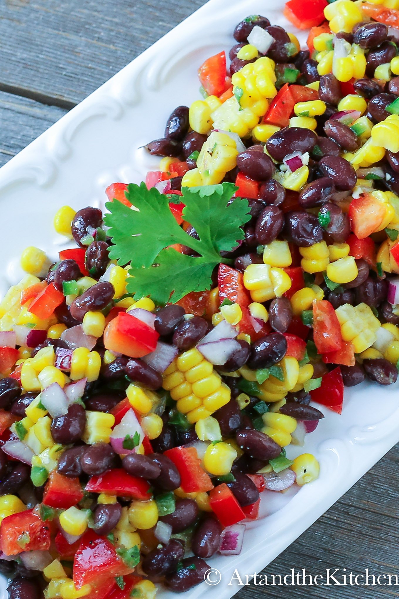 White plate filled with Santa Fe salad made with black beans, corn red , pepper, red onions and jalapeño. Garnished with parsley sprig.