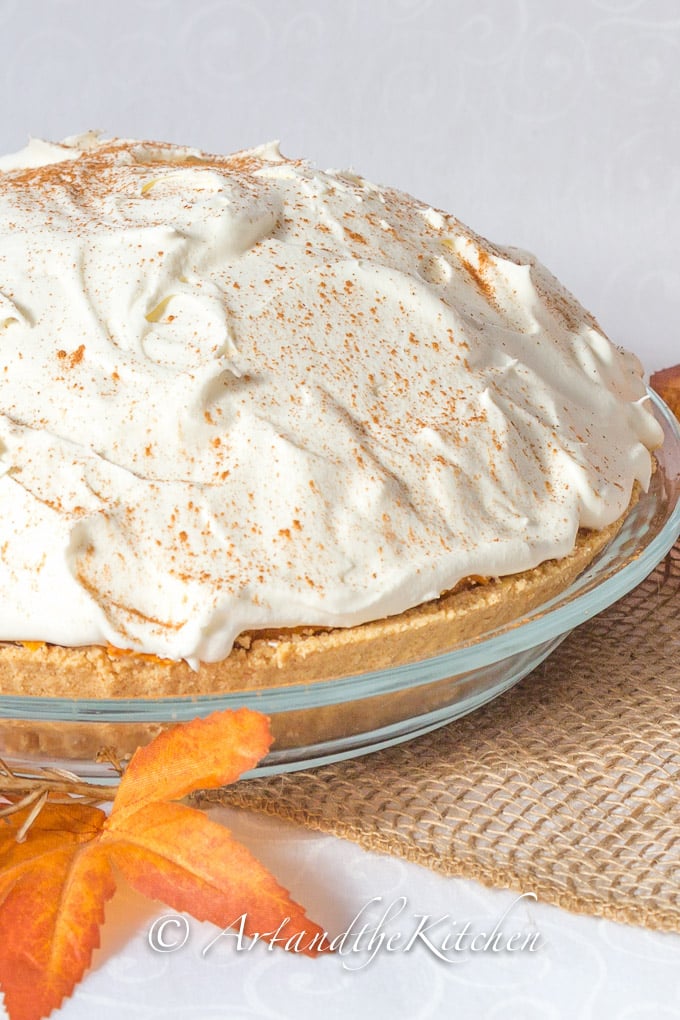 No Bake pumpkin pie topped with whipped cream, sprinkled with cinnamon with graham crust made in clear glass pie plate.
