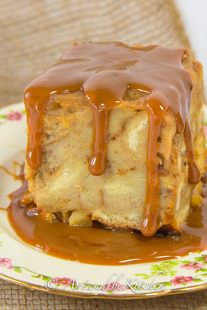 Slice of apple bread pudding covered with dulce de leche sauce on decorative plate.