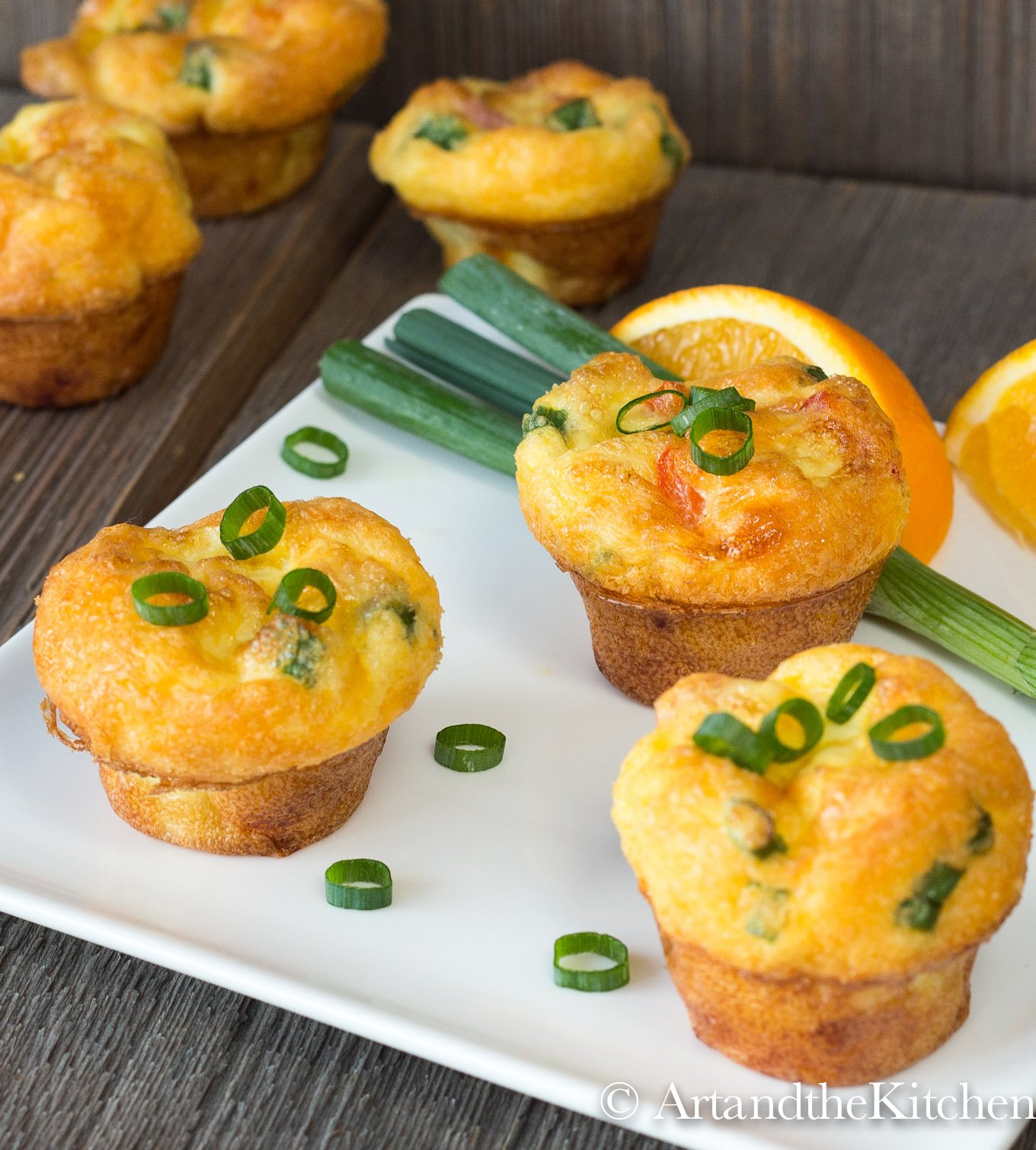 Three mini egg muffins on white plate with orange slices and green onion garnishes.