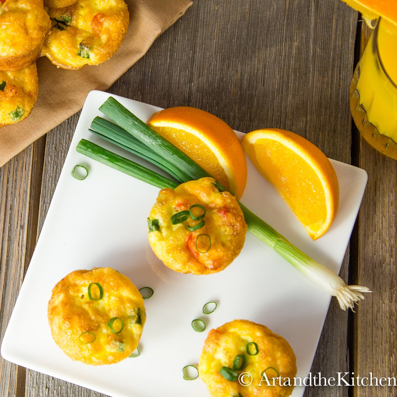 Square white plate with 3 egg bites, garnished with a green onion and orange sections.
