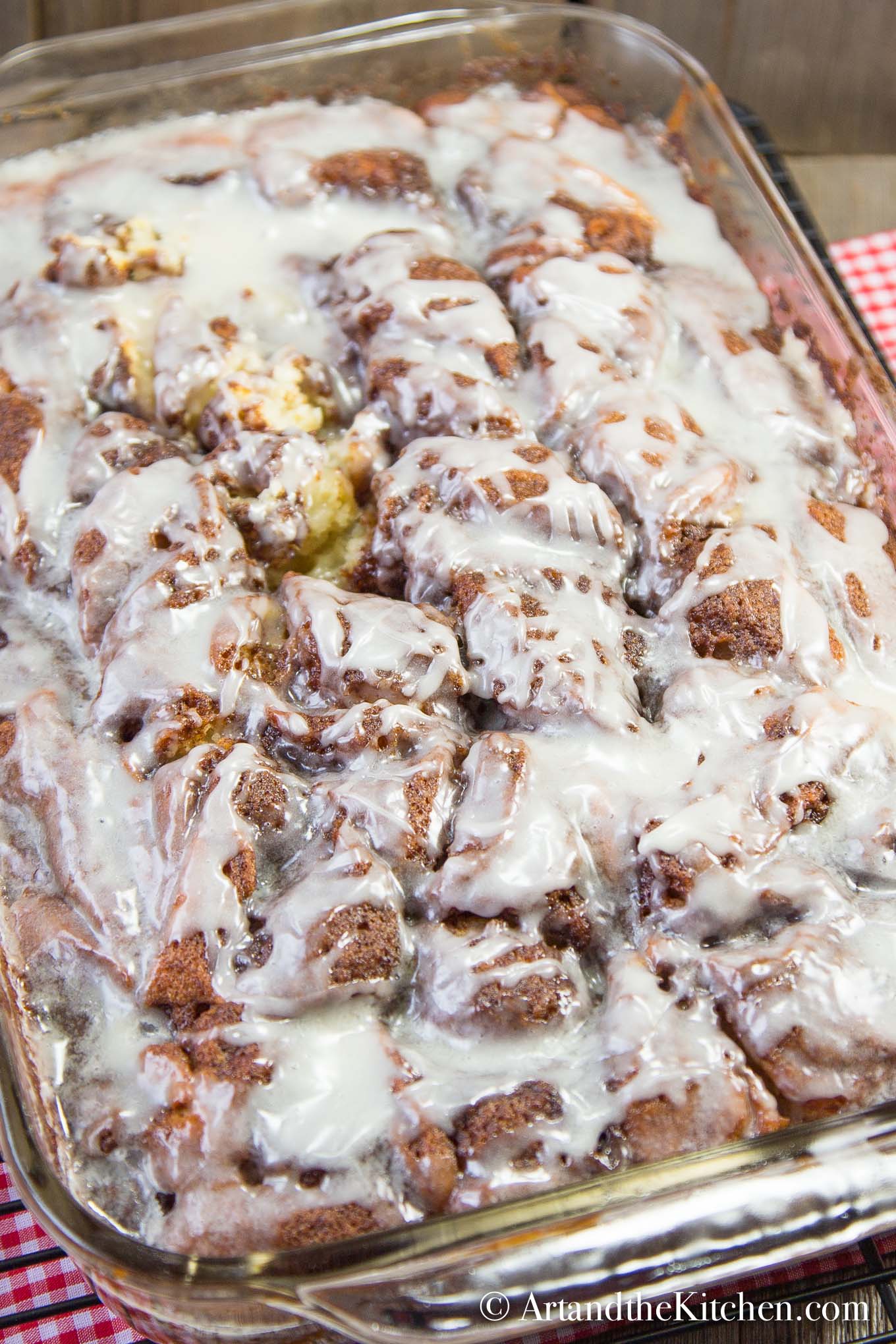 Large glass cake pan of cinnamon cake covered with white glaze.