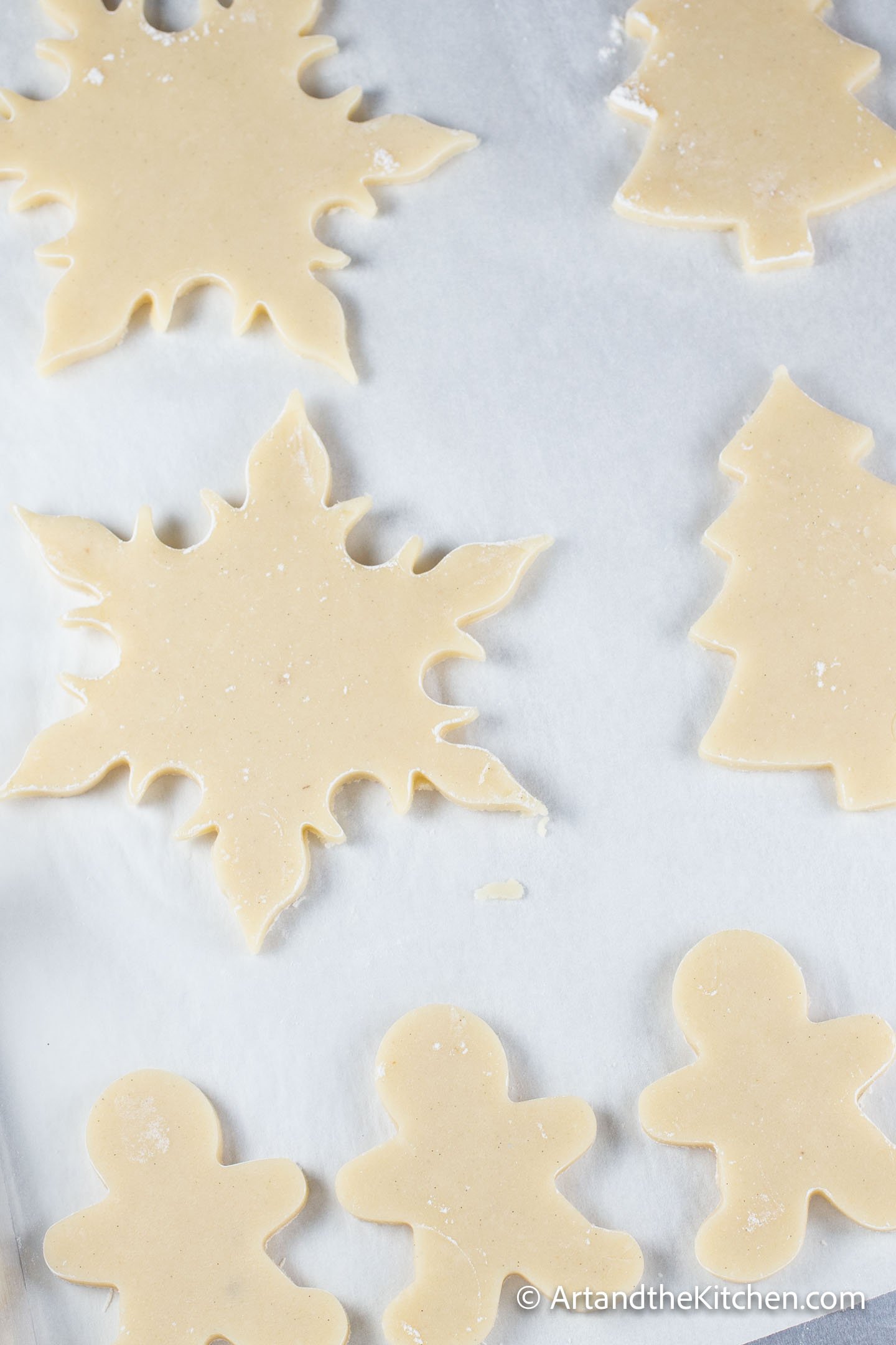 White parchment line baking pan filled with holiday shaped unbaked cookies.