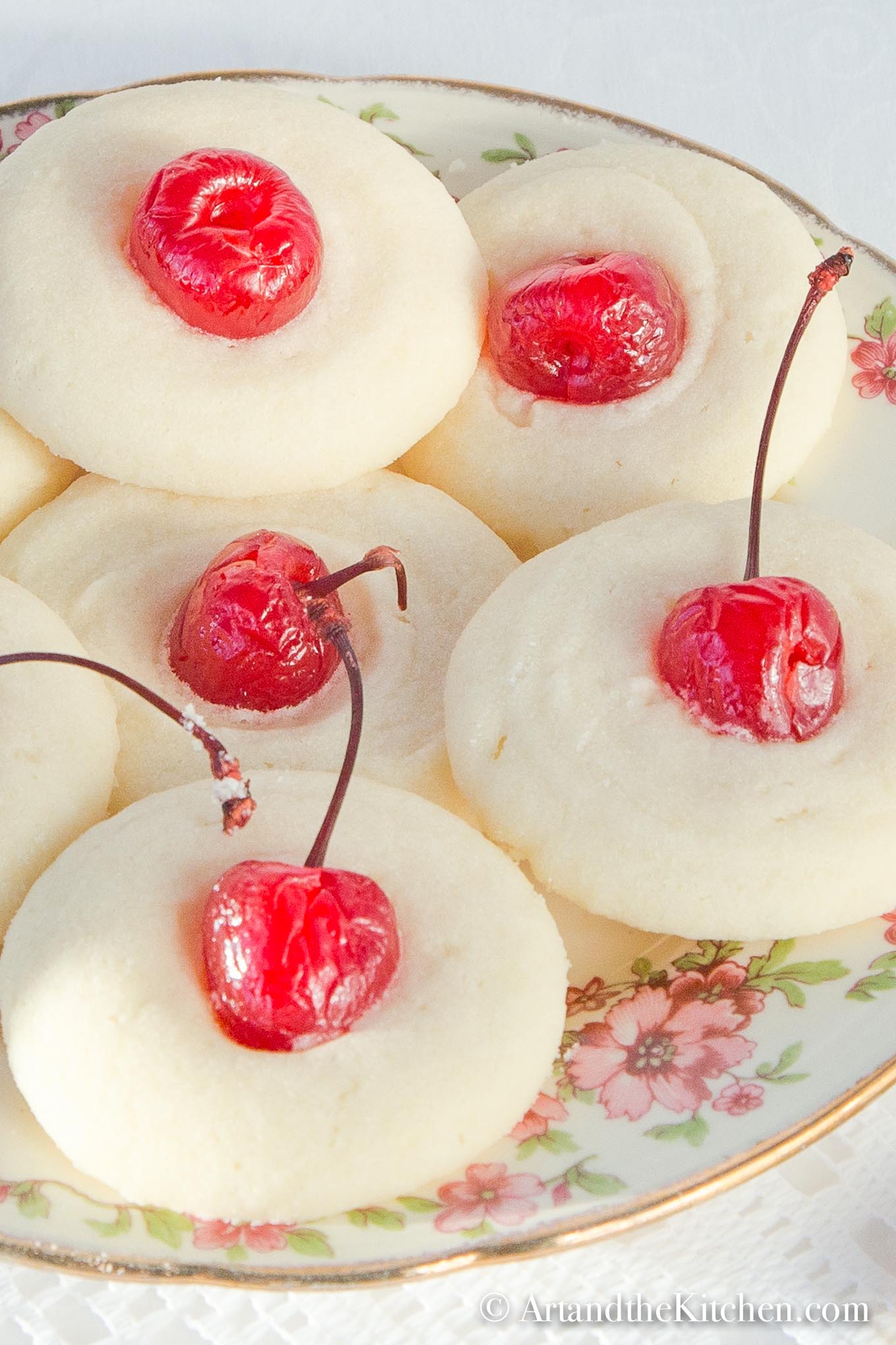 Decorative plate filled with shortbread cookies topped with maraschino cherries.