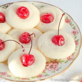 Decorative plate filled with shortbread cookies topped with maraschino cherries.