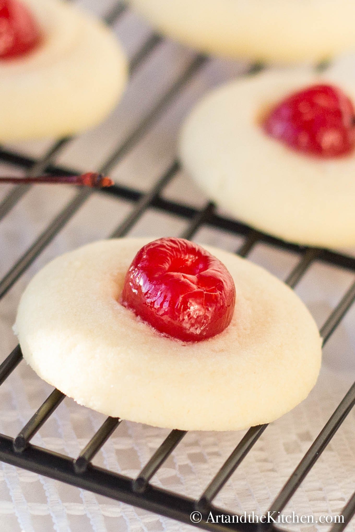 Baking rack filled with fluffy shortbread cookies topped with maraschino cherries.