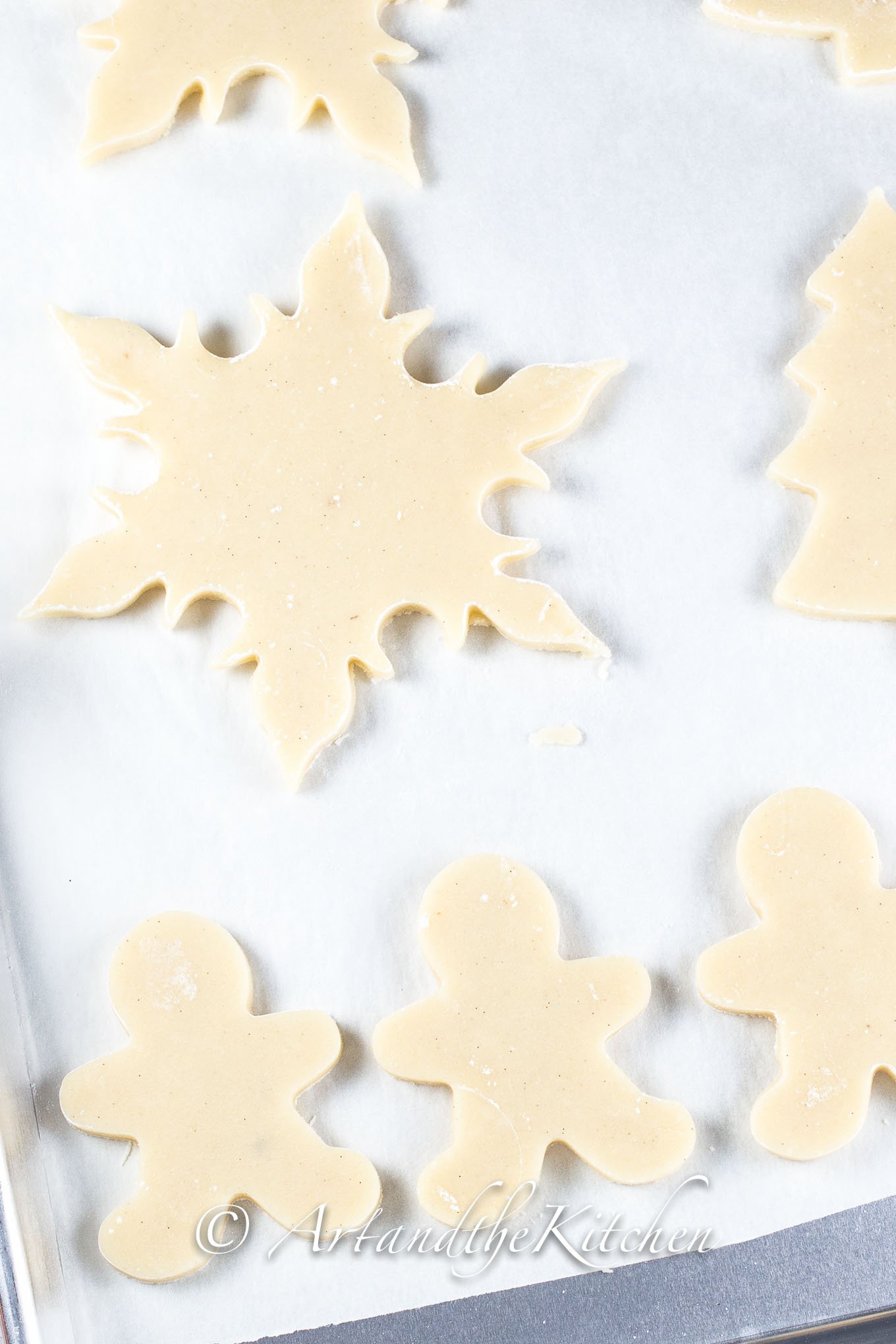 Cookie dough cut out with Christmas Cookie shapes on white parchment lined baking sheet.