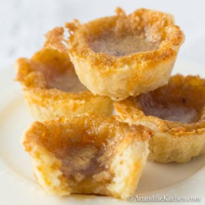 Stack of four homemade tarts with syrupy filling on white plate.