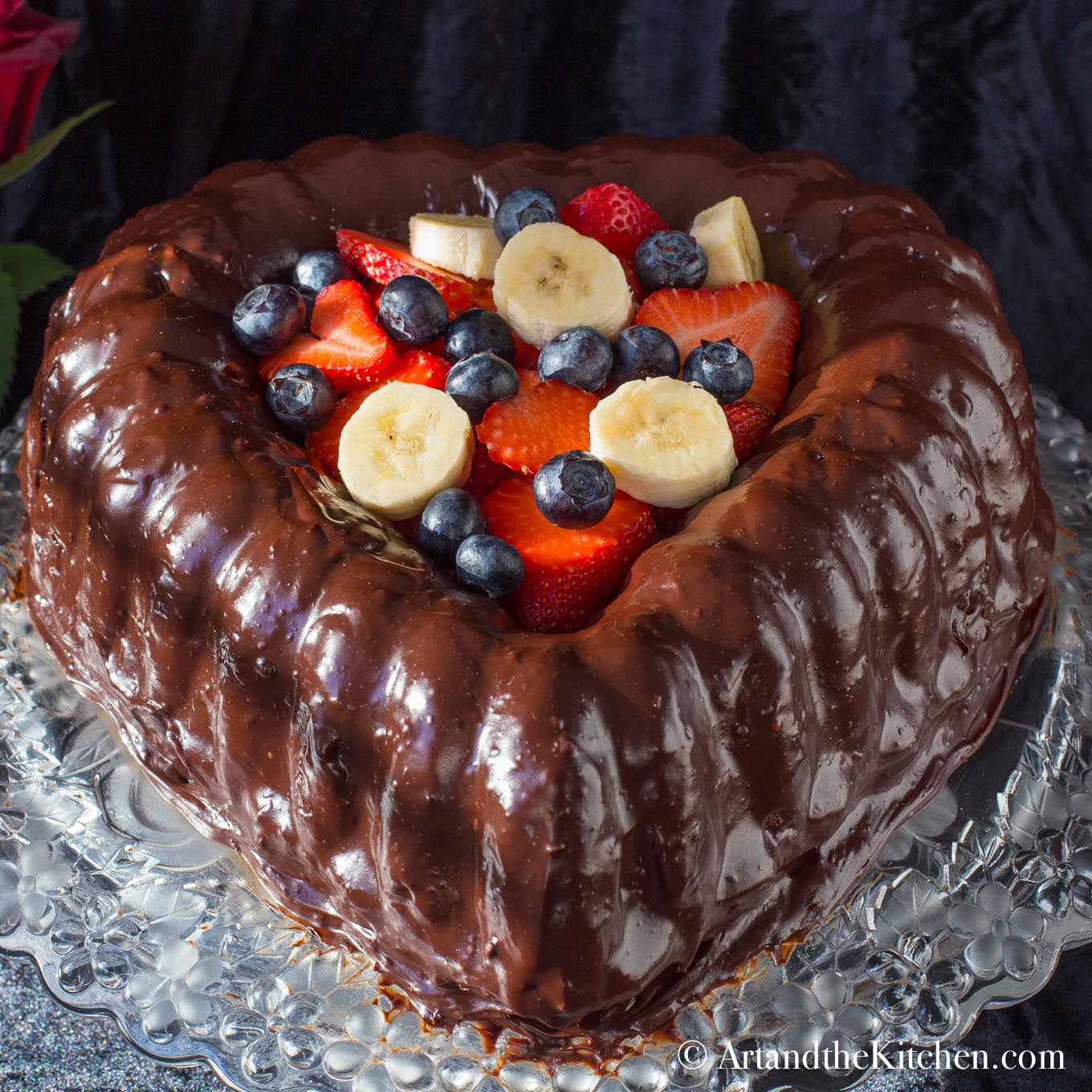 Heart shaped chocolate cake covered in chocolate ganache. Centre filled with berries and banana slices.