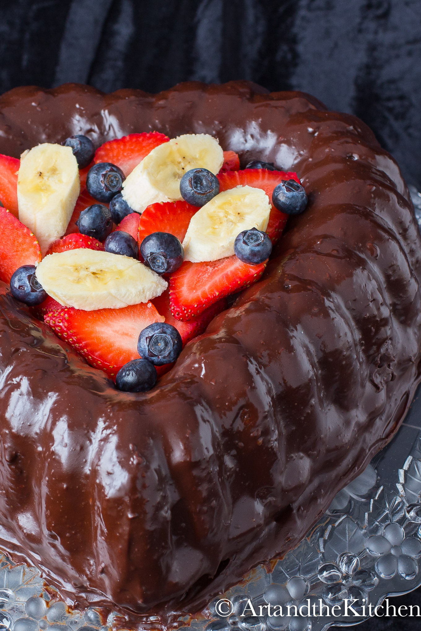 Heart shaped chocolate cake covered in chocolate ganache. Center filled with berries and banana slices.