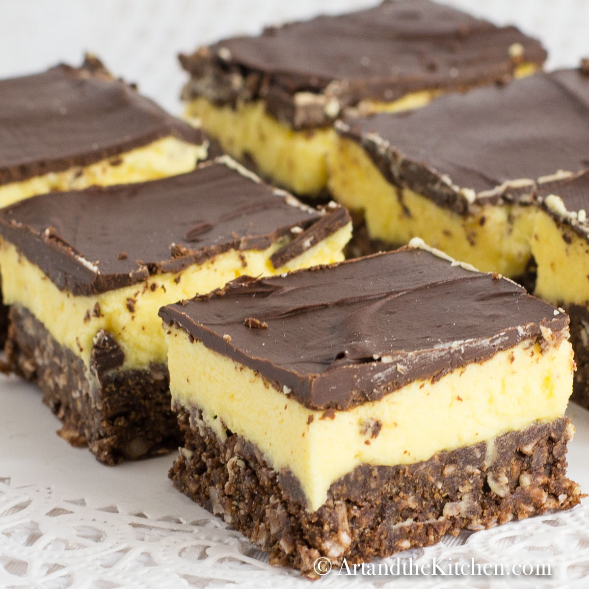 Rows of cut up squares that have layers of chocolate, yellow custard and chocolate coconut