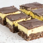 Rows of cut up squares that have layers of chocolate, yellow custard and chocolate coconut crust.