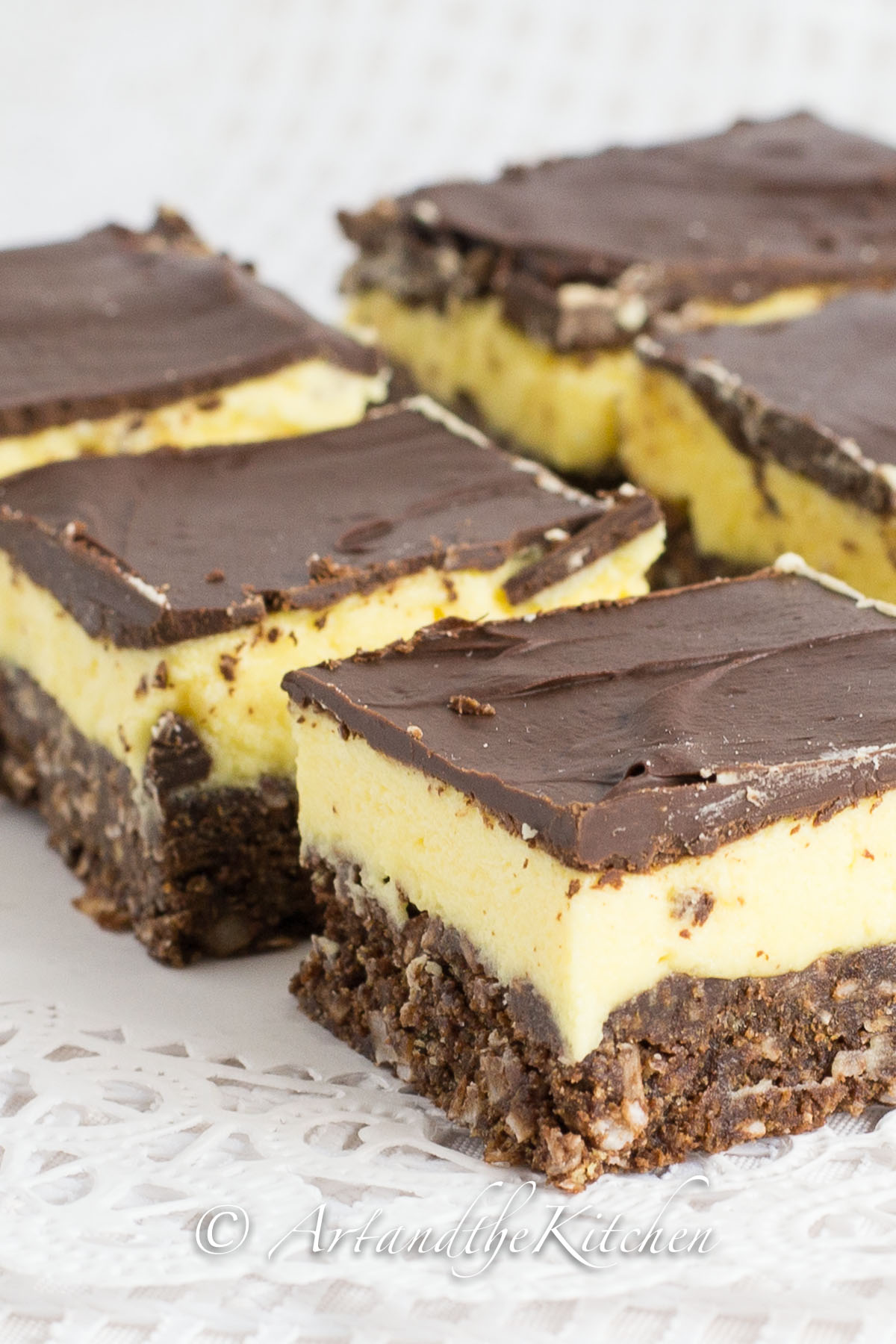 Rows of cut up squares that have layers of chocolate, yellow custard and chocolate coconut crust.