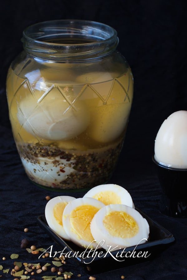 Glass jar filled with pickled eggs and brine with sliced egg on plate.
