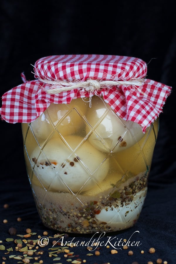 Glass jar filled with pickled eggs and brine with decorative red plaid cloth covered lid.