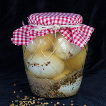 Glass jar filled with pickled eggs and brine with decorative red plaid cloth covered lid.