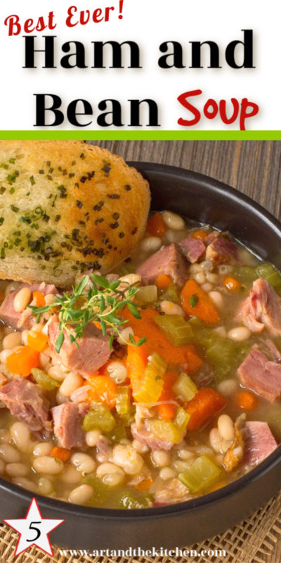 bowl of ham and bean soup with chunks of ham, navy beans, carrots and celery. Garlic bread on side of bowl, garnishes with thyme sprig.