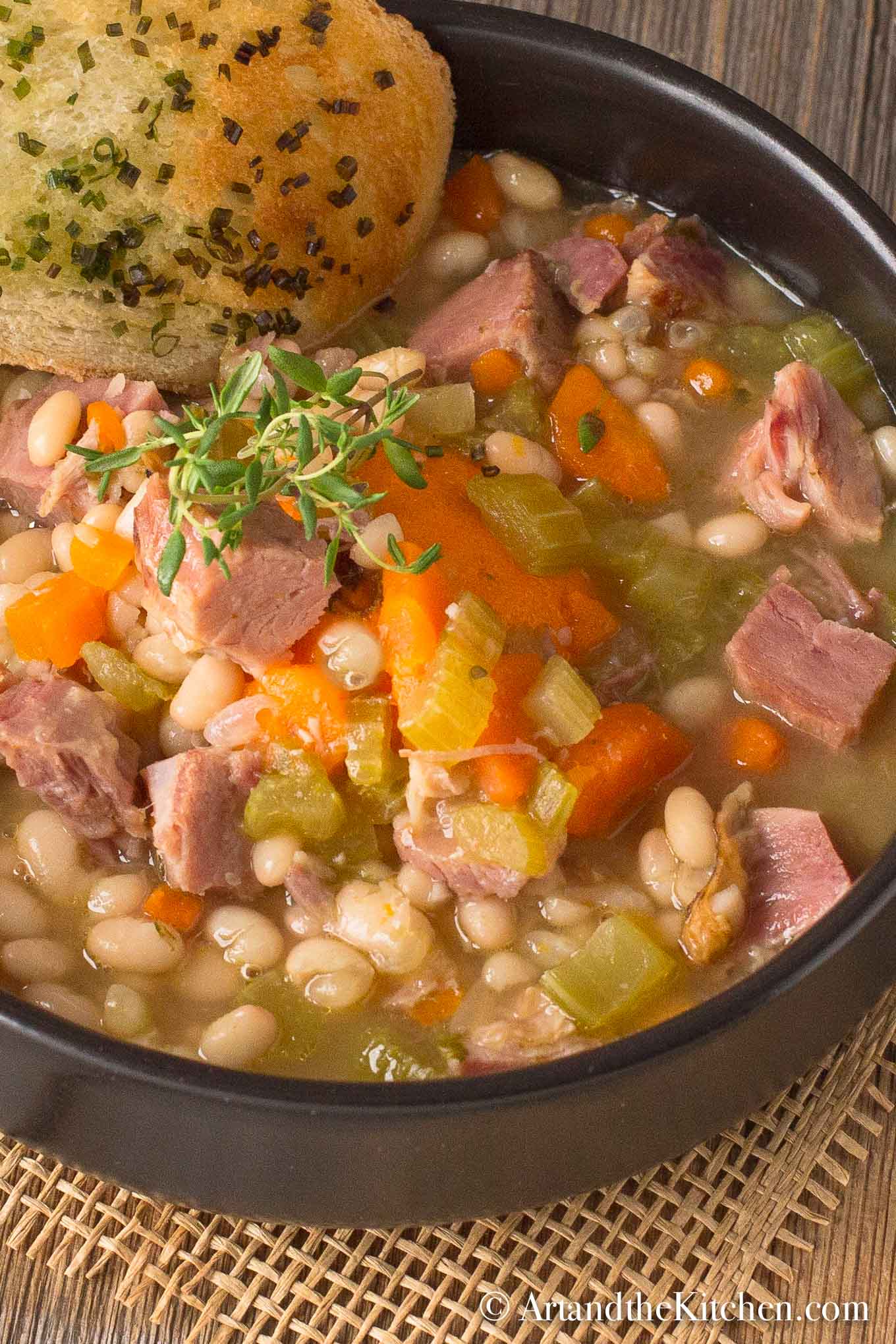 Black bowl filled with chunky soup of ham and beans with side of garlic toast.